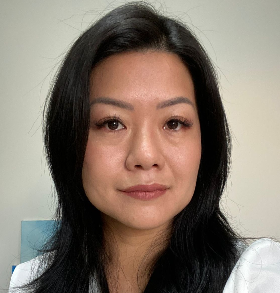 Foto de Clarissa Okino Delgado, com cabelo longo e preto, vestindo uma camisa branca, em um ambiente iluminado e acolhedor.