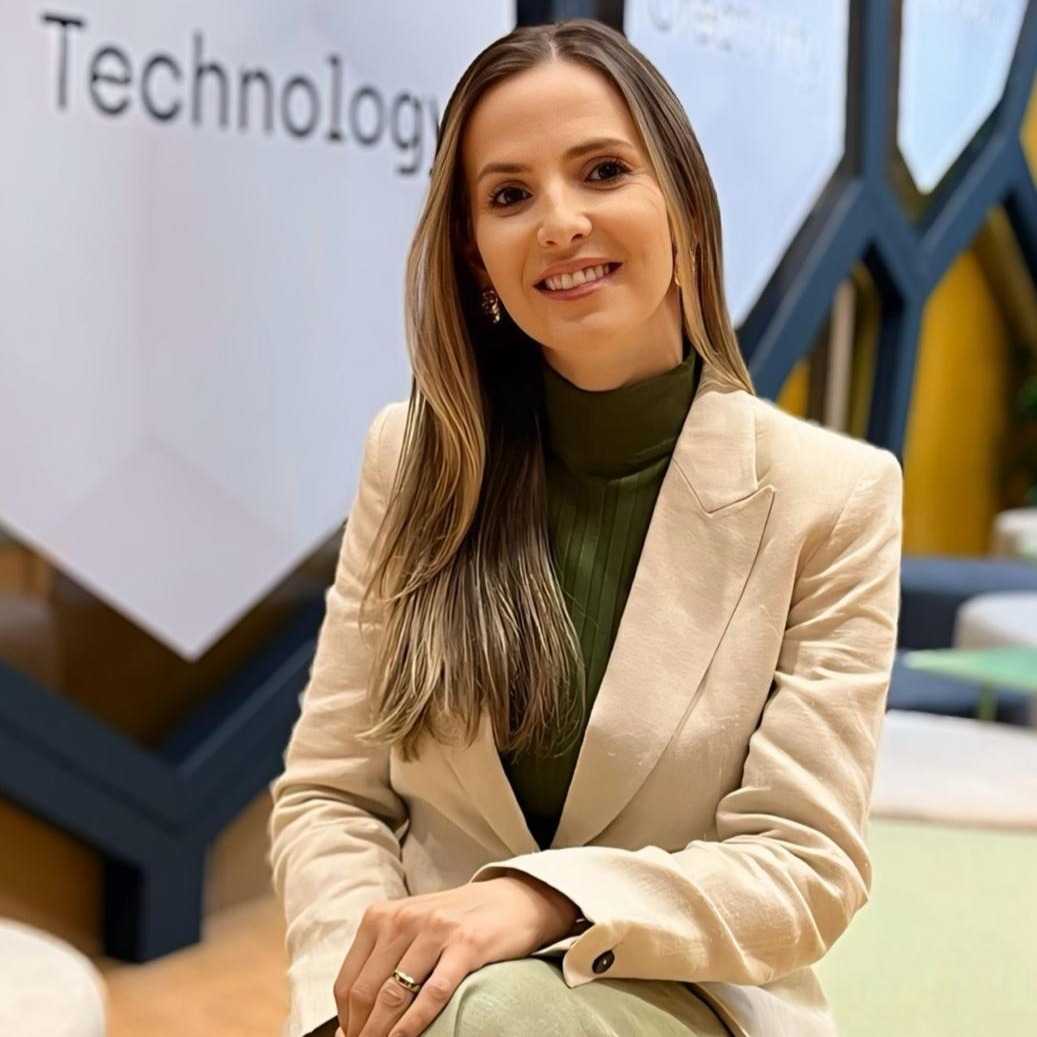 Foto de Sabrina Ciane Condi, com cabelos longos e escuros, sorrindo e olhando diretamente para a câmera.